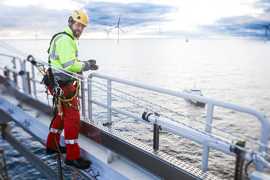 Offshore wind turbine technician in full safety gear standing on a platform with offshore wind turbines in the background